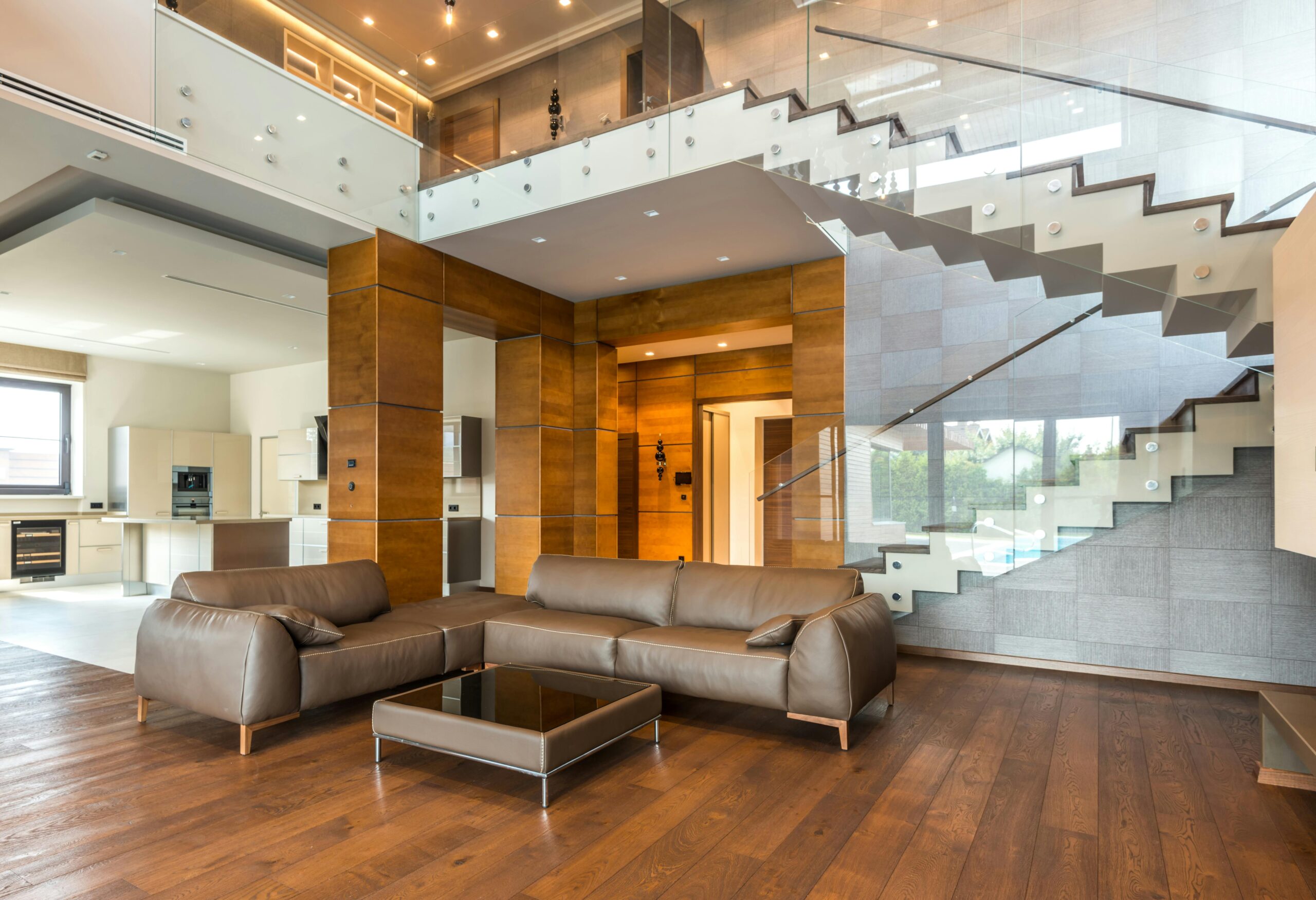 Spacious modern living room with leather sofas and a glass staircase, showcasing luxury interior design.
